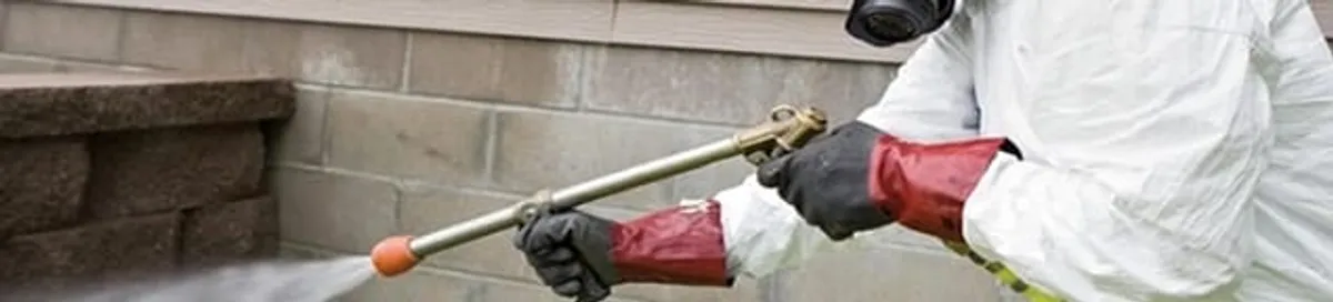 Pest control technician applying exterior insect treatment along a home foundation in Gilbert, AZ