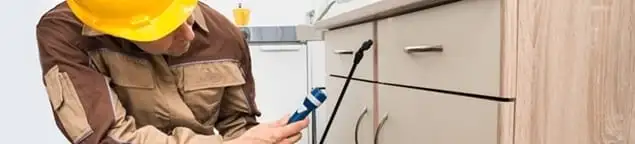 Roach exterminator applying treatment under kitchen cabinets in Gilbert, AZ