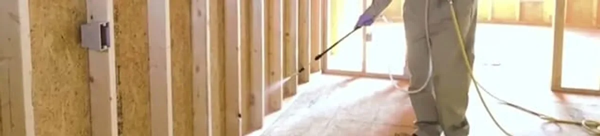 Termite treatment technician applying spray along framing and unfinished walls in Gilbert, AZ