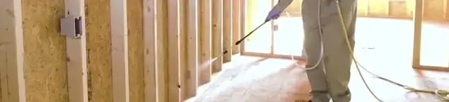 Termite treatment technician applying spray along framing and unfinished walls in Gilbert, AZ