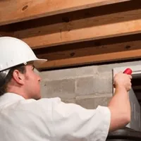 Termite inspection technician checking a basement wall and framing for termite activity in Gilbert, AZ